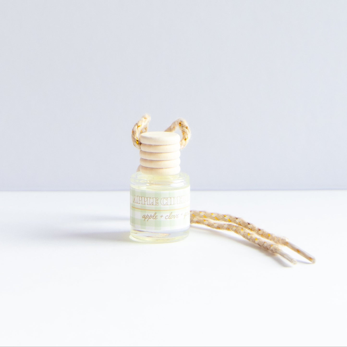 A small glass diffuser bottle with a light wood reed stopper and a beige patterned cord, labeled 'apple & citrus', on a clean white surface against a light gray background.