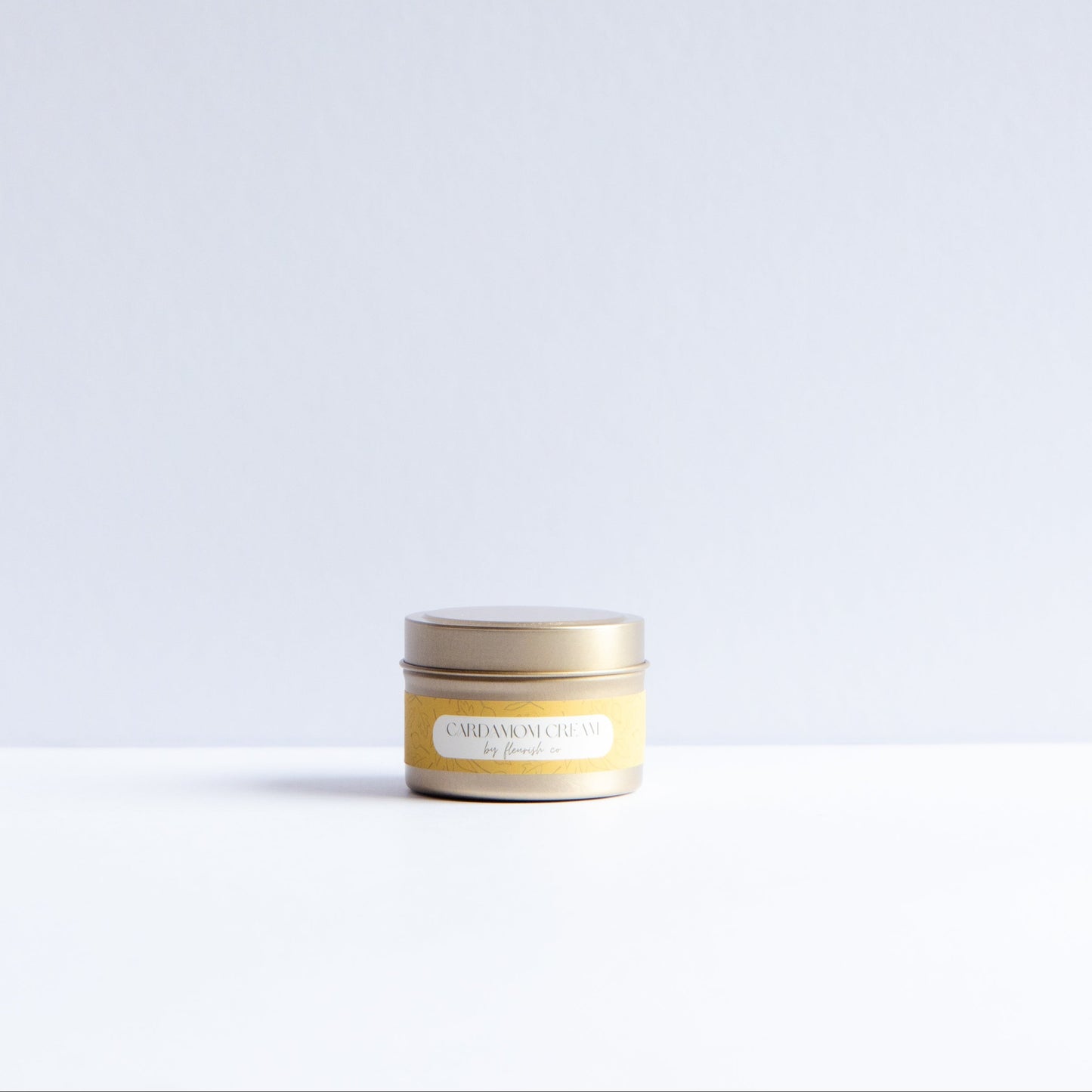 A small round tin candle with a gold lid and a pale yellow label reading 'CITRON MANGROVE' and 'SANDWICH FLAVOR' on a white surface against a light gray background.