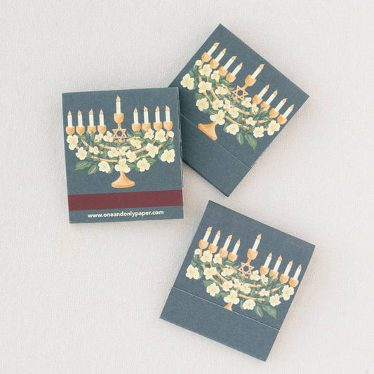 Three small matchbooks with Menorah designs on a light gray background