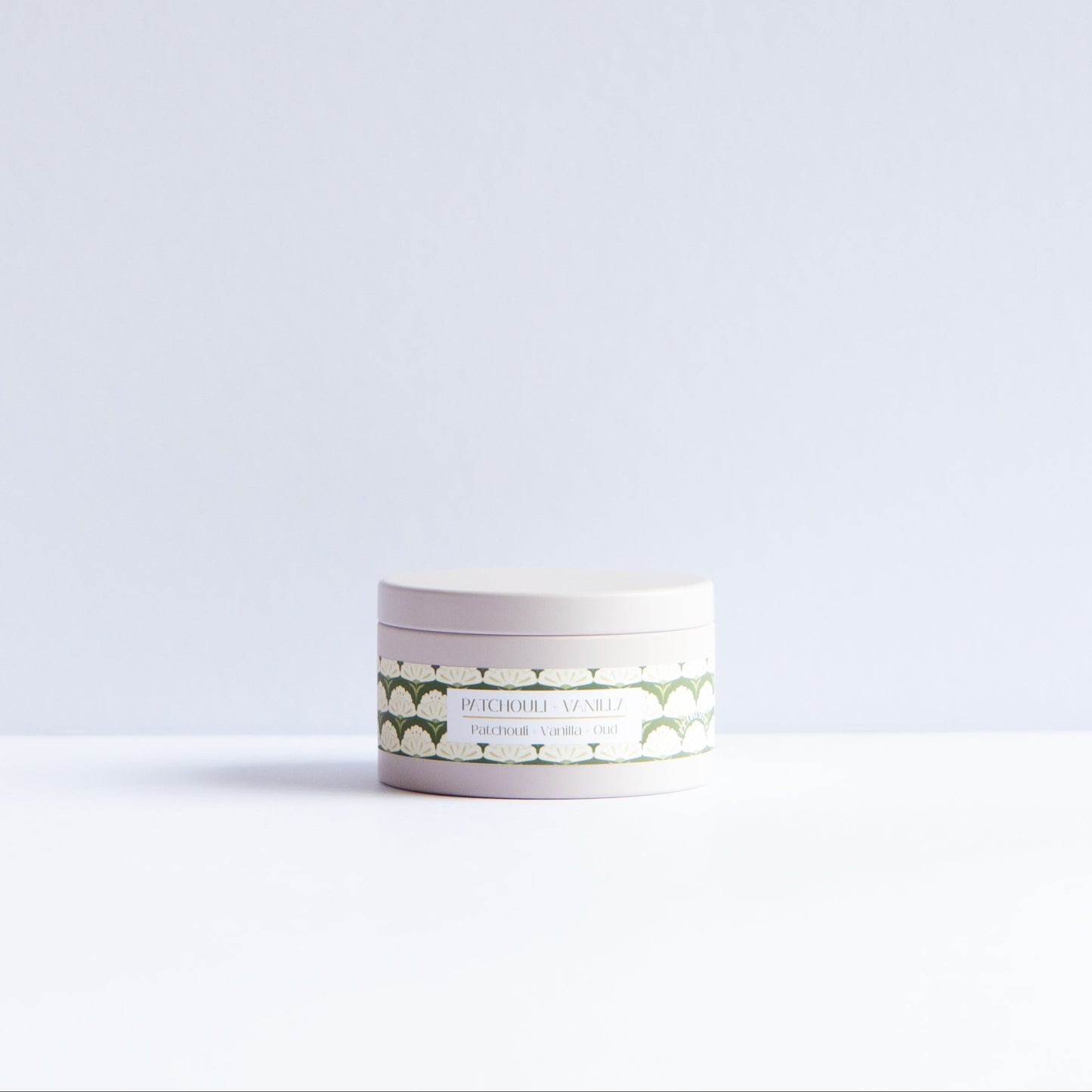 A small round cosmetic jar with a white lid and a white label featuring a green geometric pattern, set on a white surface against a light gray background.