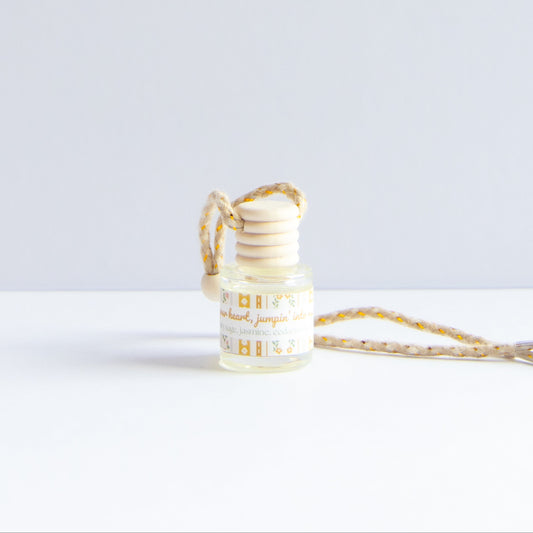 A small glass reed diffuser bottle with a white wooden stopper and a patterned beige-and-yellow cord, shown on a clean white surface against a light gray background.