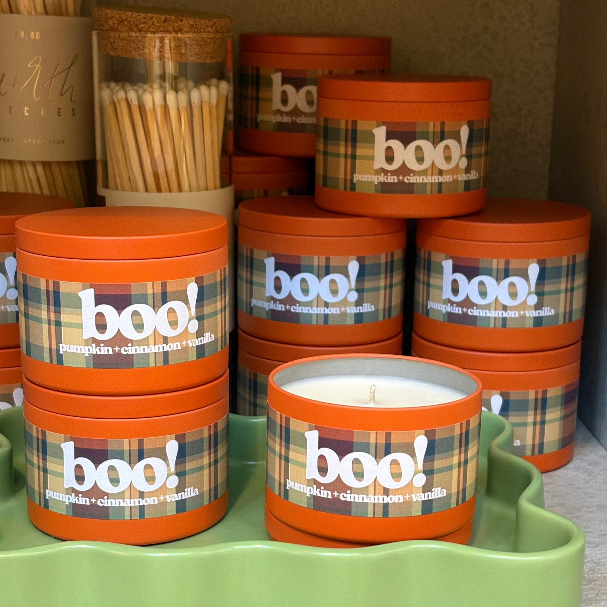 Stacks of 'boo!' themed candles on a green tray with plaid labels.