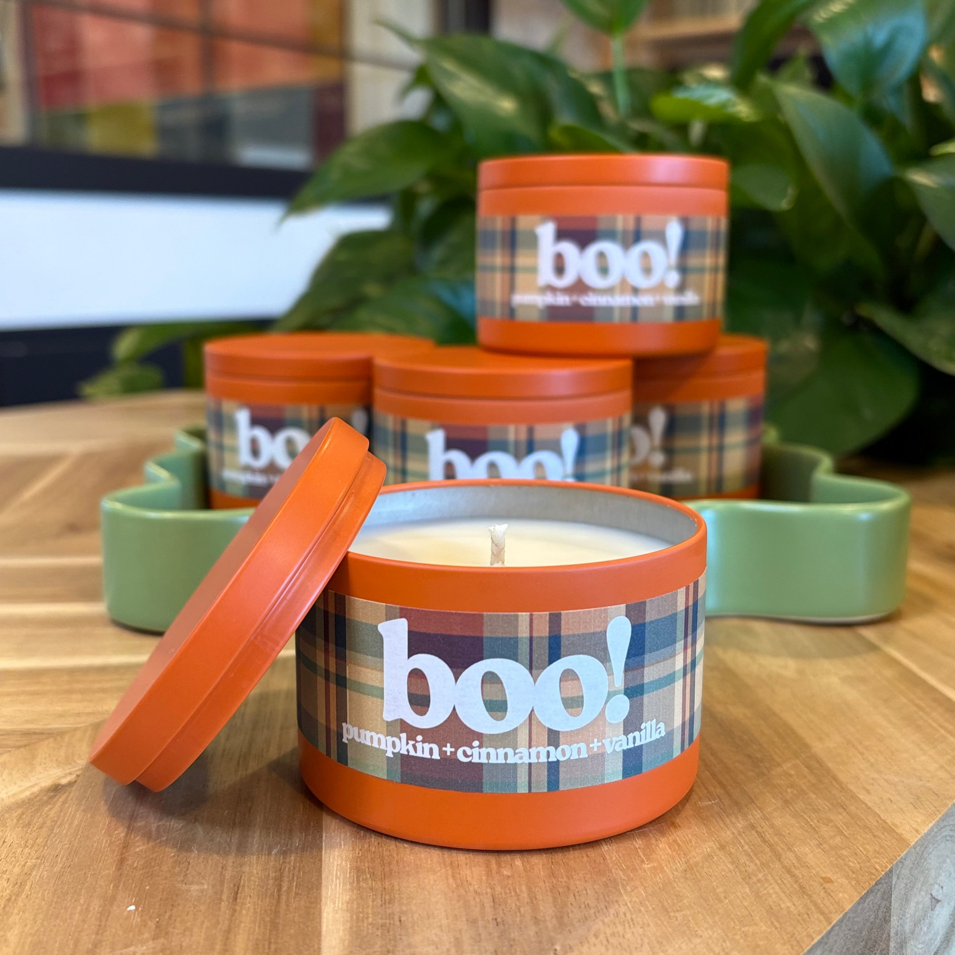 Candle with 'boo!' label on a wooden surface with plants in the background