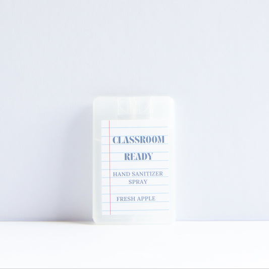 A small clear plastic bottle of Classroom Ready Hand Sanitizer Spray in Fresh Apple scent, standing upright on a white surface against a light gray background.