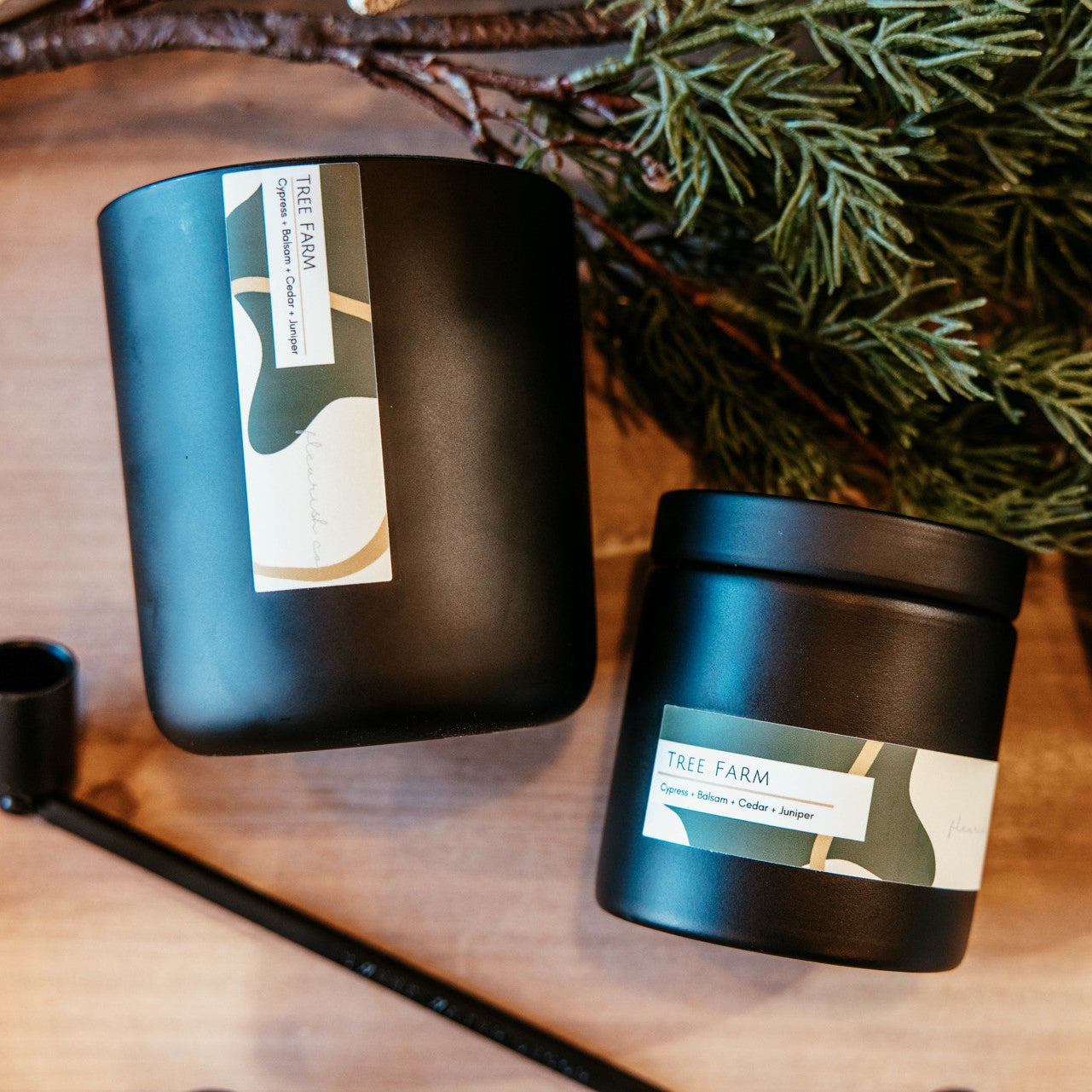 Three black containers with labels on a wooden surface with greenery in the background