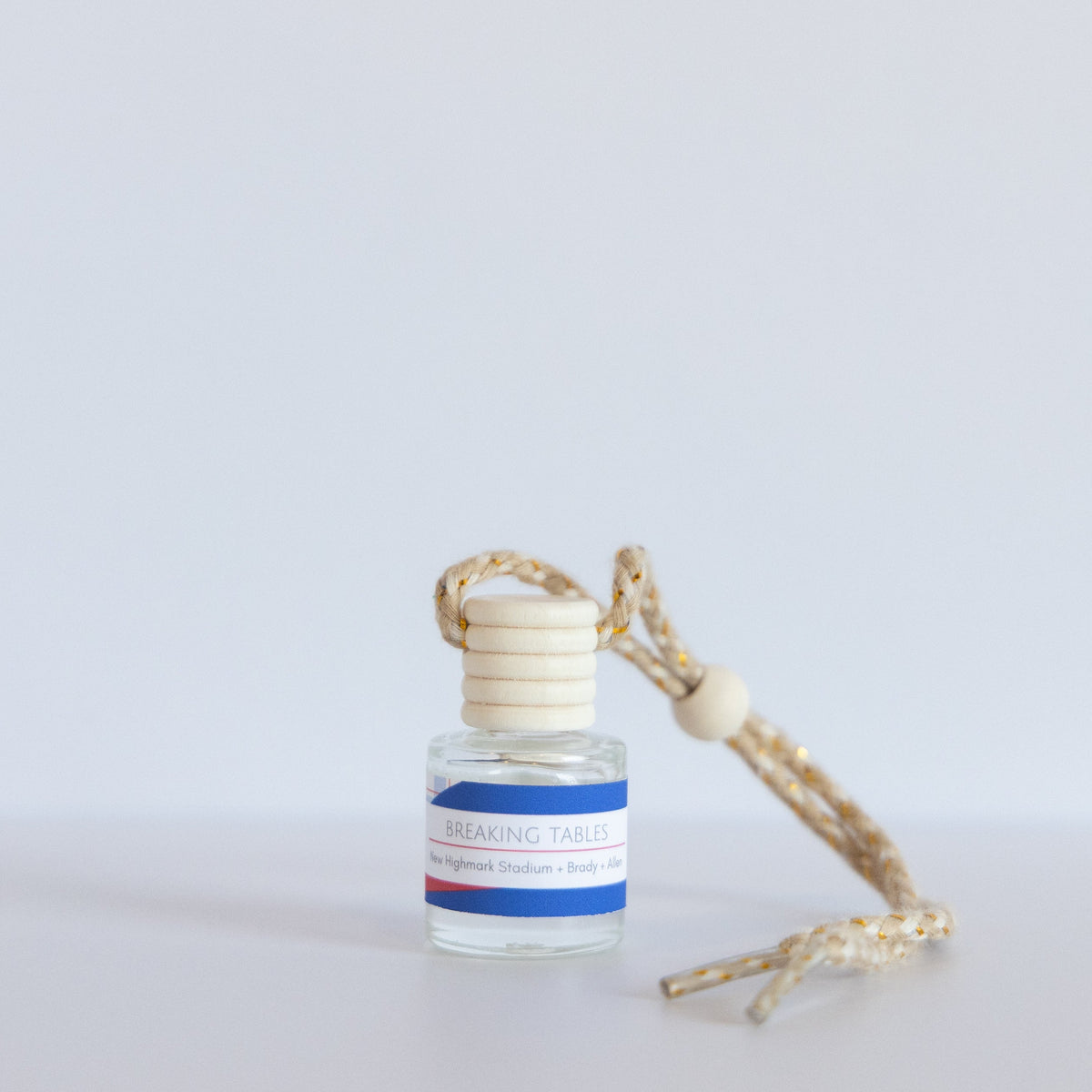 A small glass reed diffuser bottle with a cream-colored wooden cap and a braided beige cord, shown on a plain light gray background.