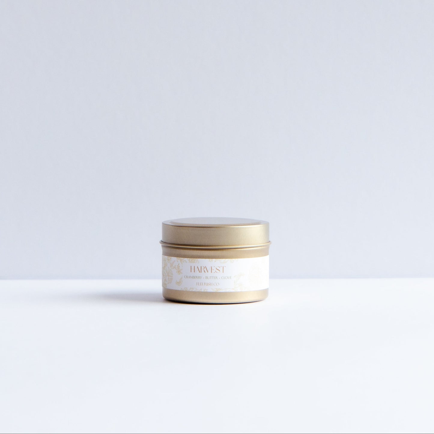 A small round cosmetic jar with a metallic gold lid and a cream-colored label, placed on a white surface against a light gray background.