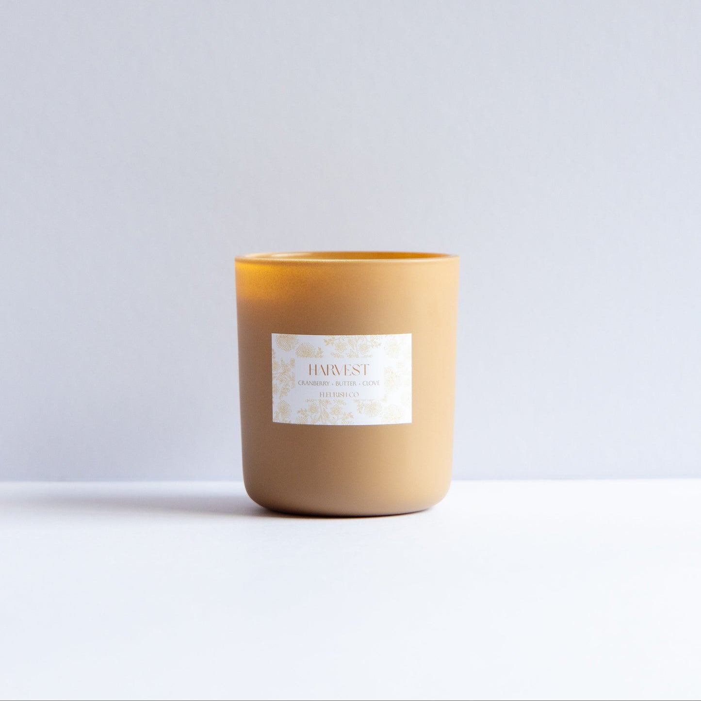 A single candle in a matte tan jar with a white label reading 'BURUST' and 'BUSTED BY BURN', set against a clean white and light gray background.