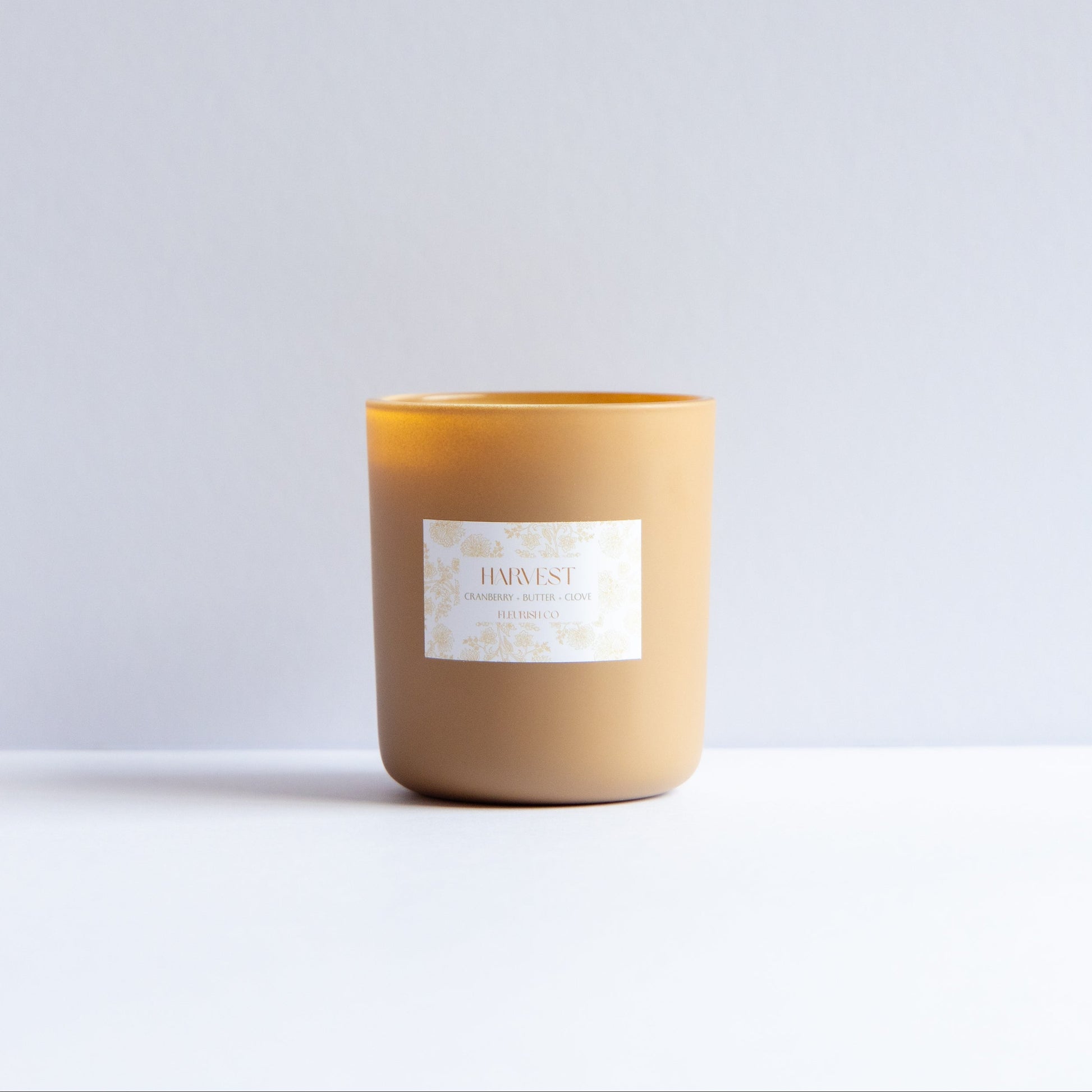 A single candle in a matte tan jar with a white label reading 'BURUST' and 'BUSTED BY BURN', set against a clean white and light gray background.