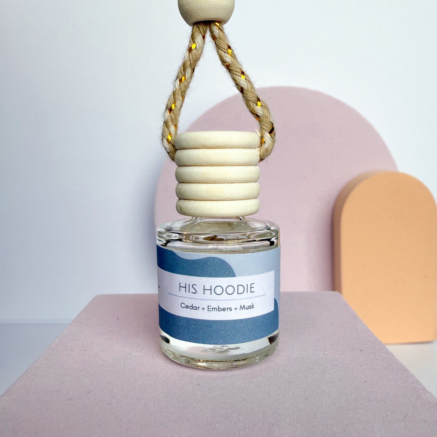 Perfume bottle labeled 'HIS HOODIE' with a wooden cap on a neutral background