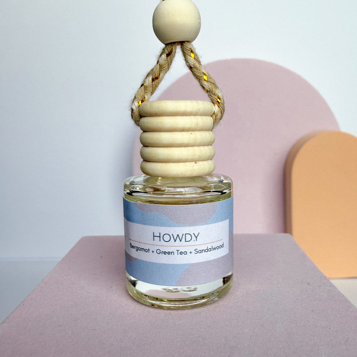 Small glass bottle with wooden cap labeled 'HOWDY' on a pink surface.