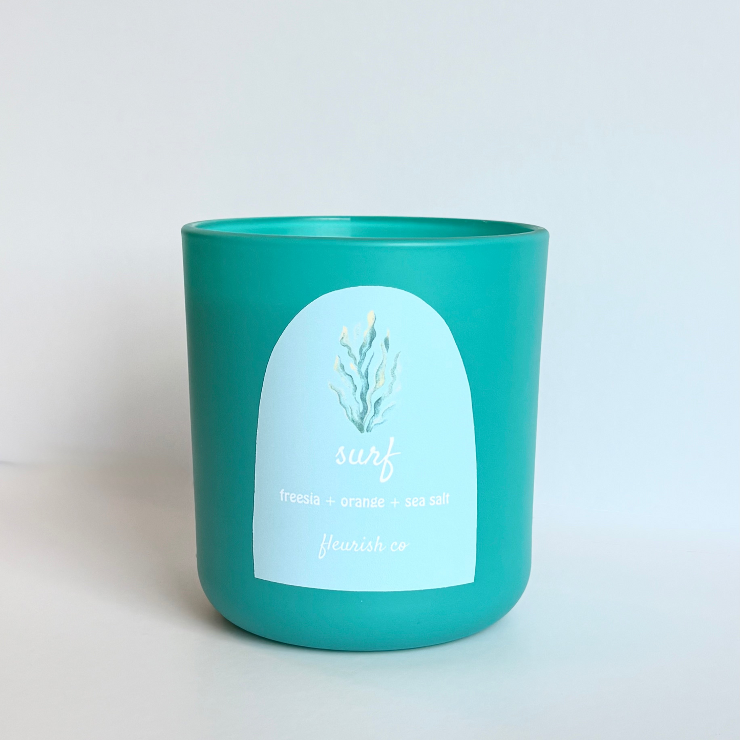 Turquoise candle with a white label on a light gray background