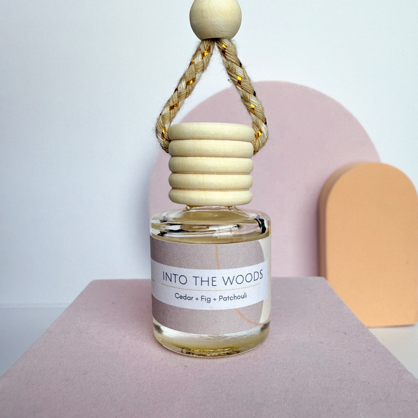Small glass bottle labeled 'Into the Woods' with a wooden cap on a pink surface.