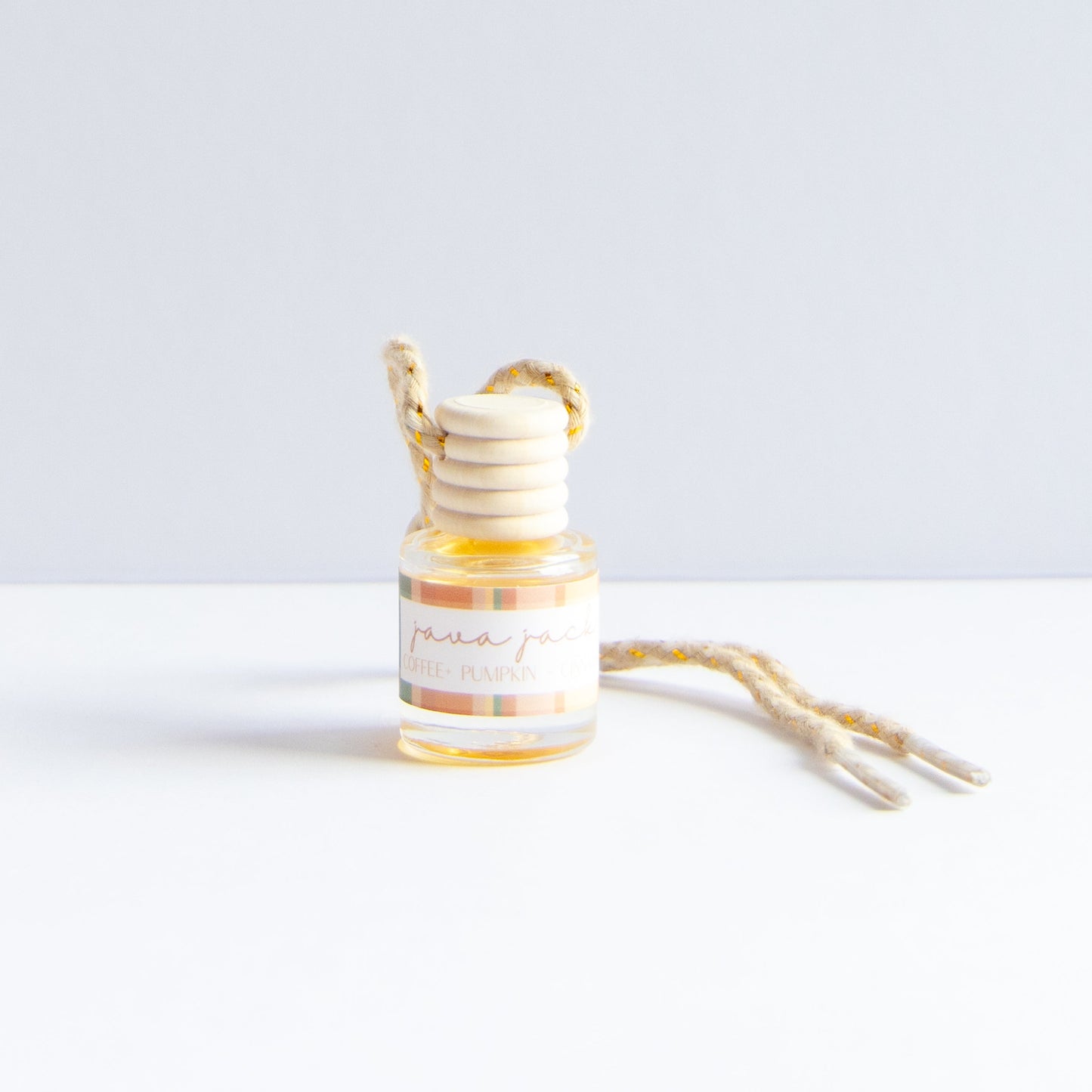 A small glass bottle with a striped label reading 'java jack' and a wooden honey dipper resting inside, with a natural jute hanging loop and cord on a white surface against a light gray background.