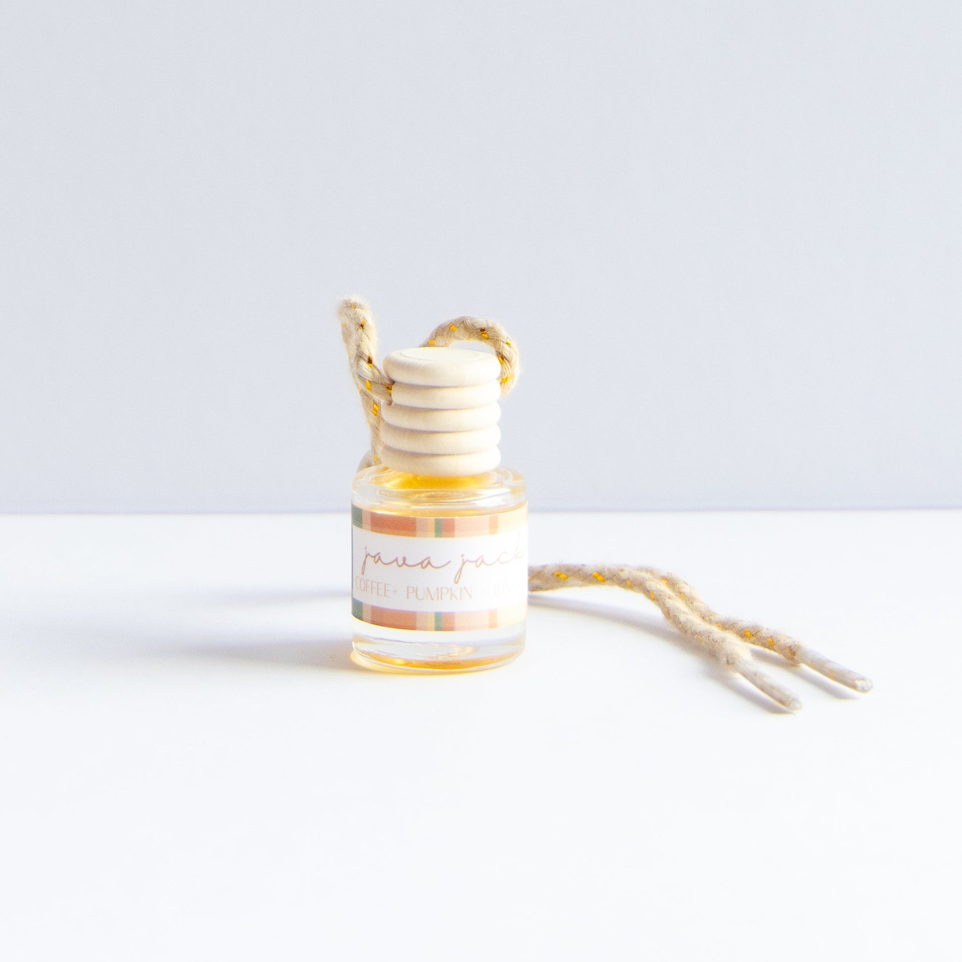 A small glass bottle with a striped label reading 'java jack' and a wooden honey dipper resting inside, with a natural jute hanging loop and cord on a white surface against a light gray background.
