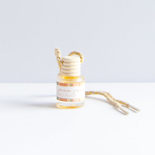 A small glass bottle with a striped label reading 'java jack' and a wooden honey dipper resting inside, with a natural jute hanging loop and cord on a white surface against a light gray background.