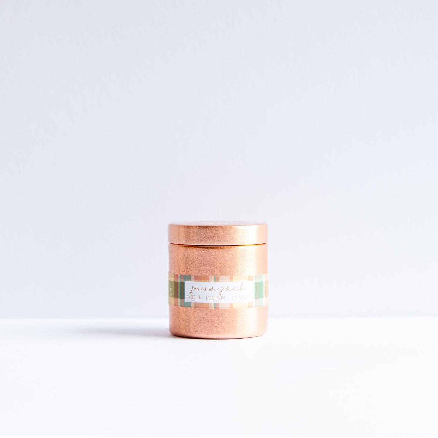 A small cylindrical tin with a metallic copper finish and a patterned label, standing on a white surface against a white background.