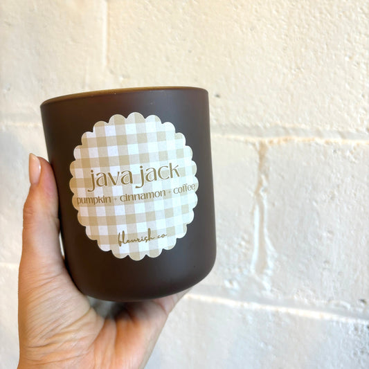 Hand holding a brown coffee cup with 'java jack' branding against a white tiled wall.