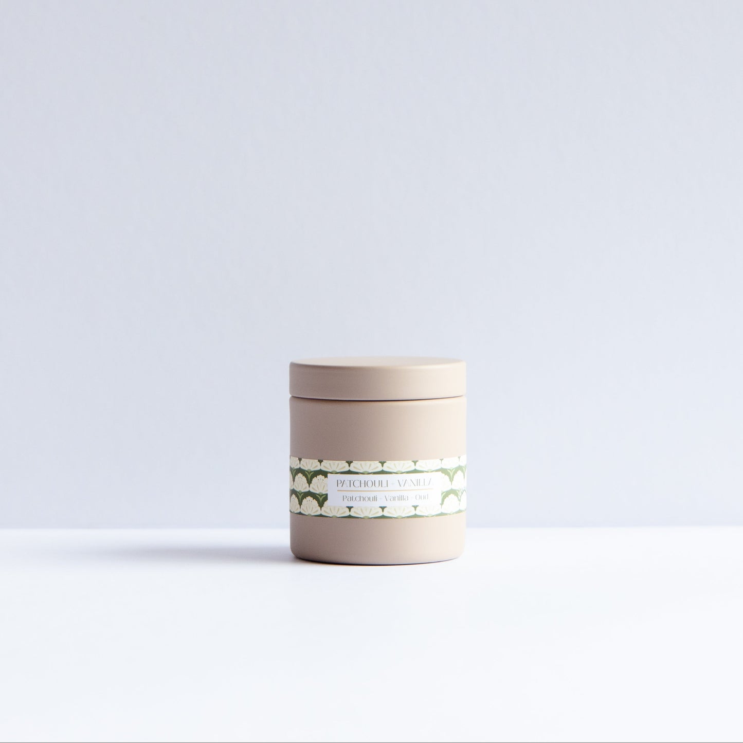 A small cylindrical beige jar with a matching lid and a decorative green and white label, centered on a clean white surface against a pale gray background.