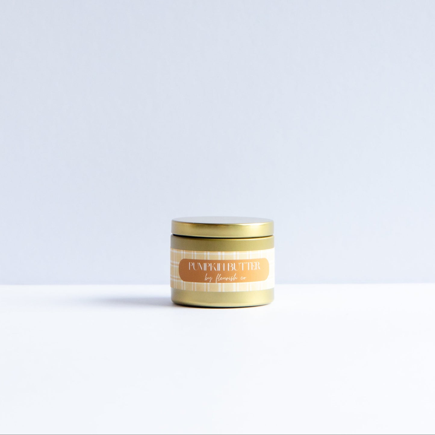 A small round tin candle with a gold lid and a cream label reading 'MYSTERY TIN' and '12 hours' on a white surface against a light gray background.