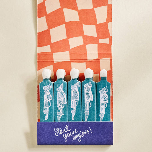 Matchbox with checkered design and matches labeled 'Start Your Engines!' on a beige background