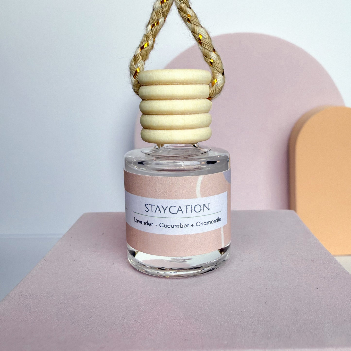 Perfume bottle labeled 'Staycation' with a wooden cap on a pink surface.