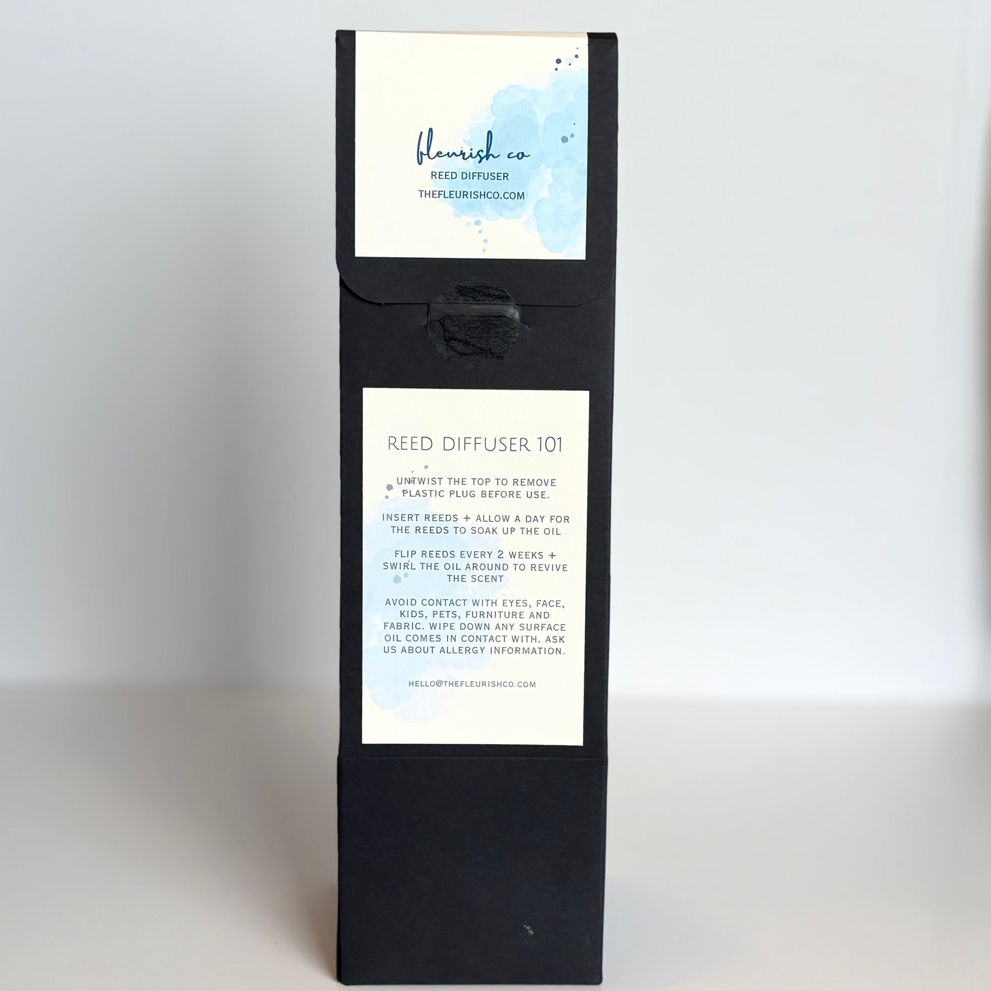 Black reed diffuser packaging with white labels on a white surface