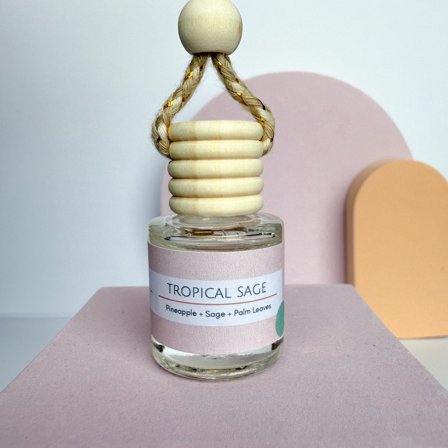 Perfume bottle labeled 'Tropical Sage' with a wooden holder on a pink surface.