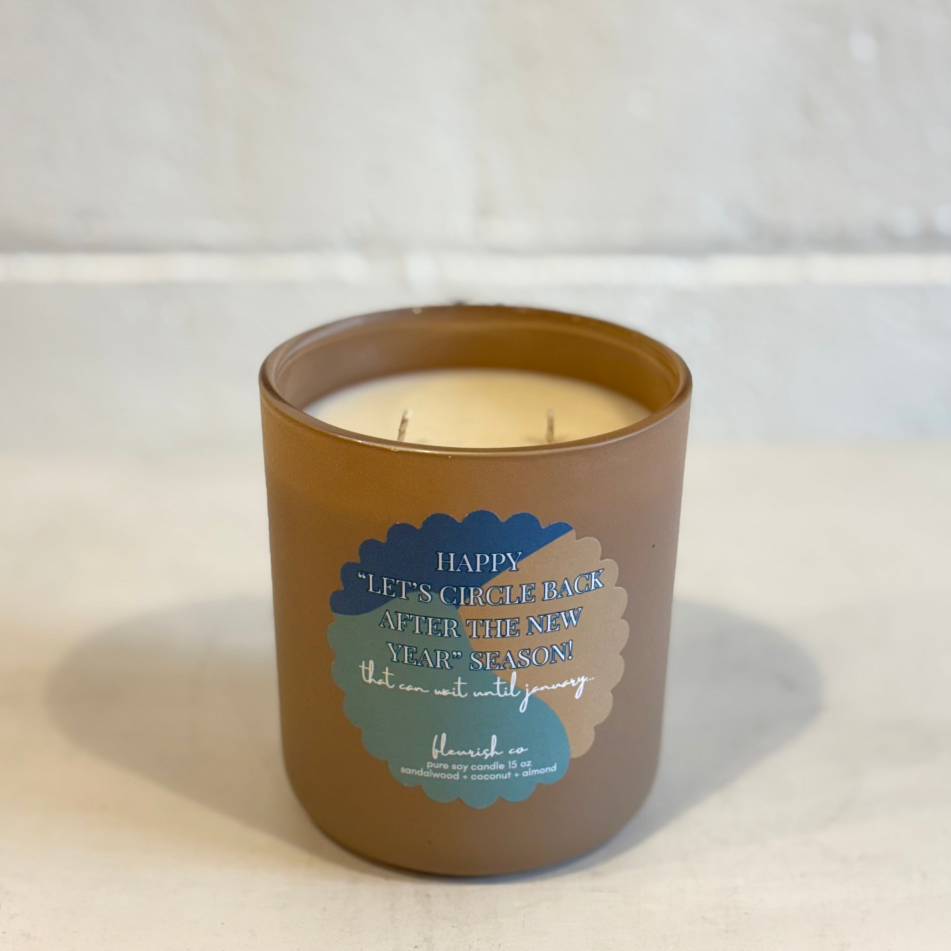 Candle in a brown jar with a label on a white surface